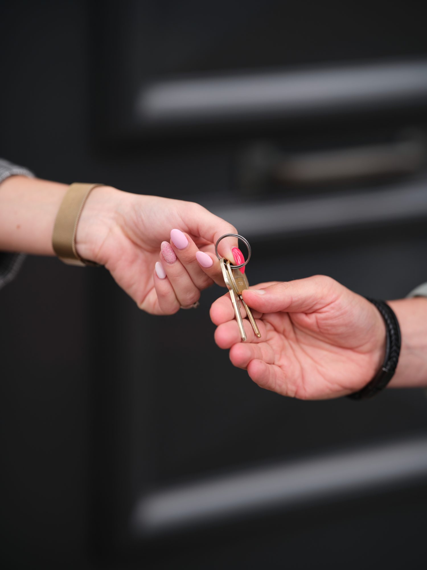 Close-up van twee handen die huissleutels overdragen voor een donkere voordeur.
