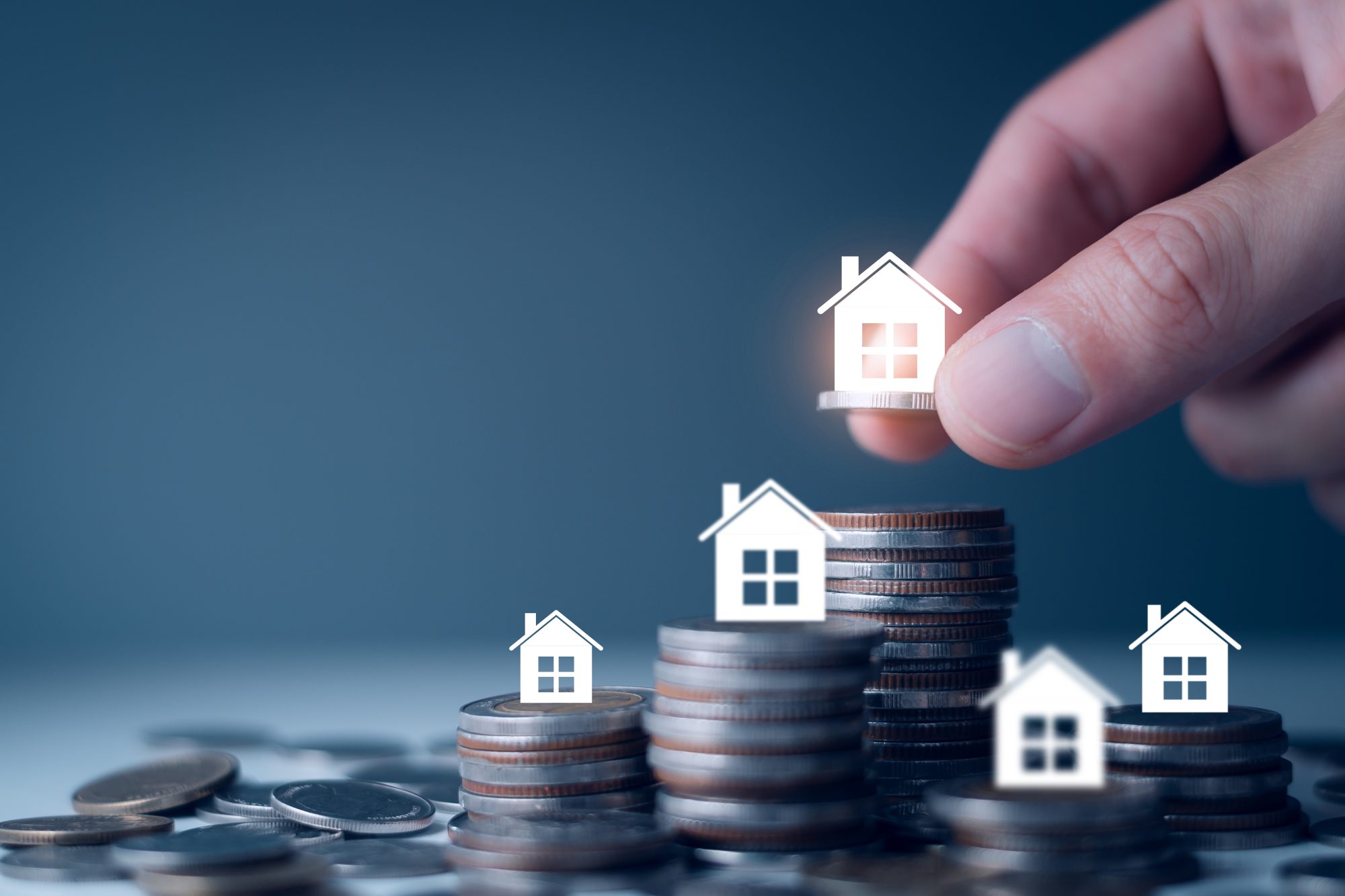 Hand plaatst miniatuurhuis op stapels munten als beeld voor woning kopen en overdrachtsbelasting.